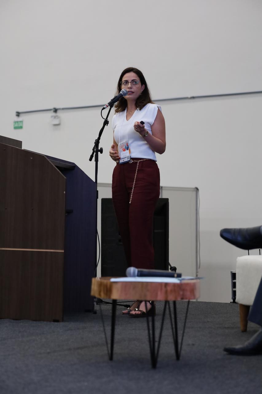 Dra. Gerusa Vilas-Bôas em pé ao microfone, durante uma palestra.