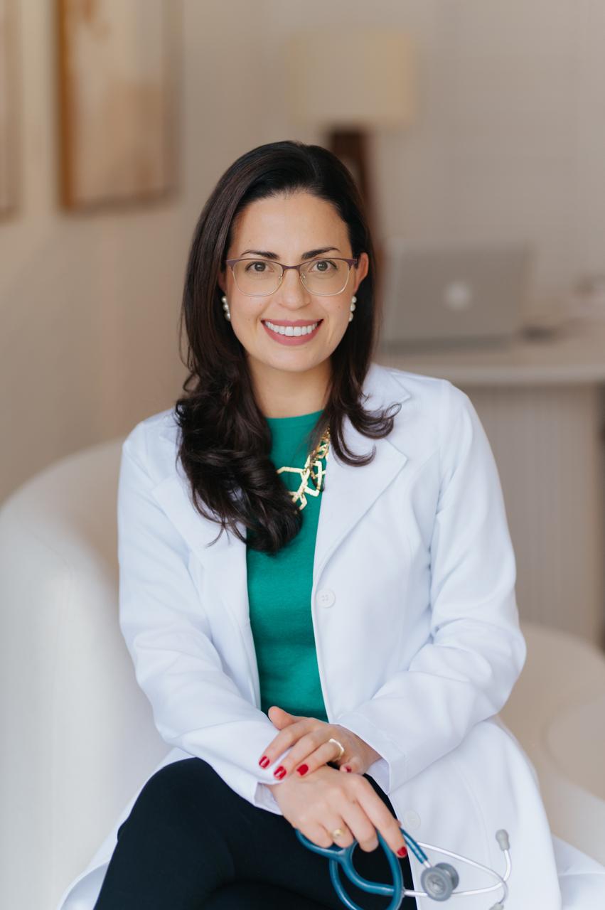 Dra. Gerusa Vilas-Bôas sentada, de jaleco branco, com o estetoscópio nas mãos.